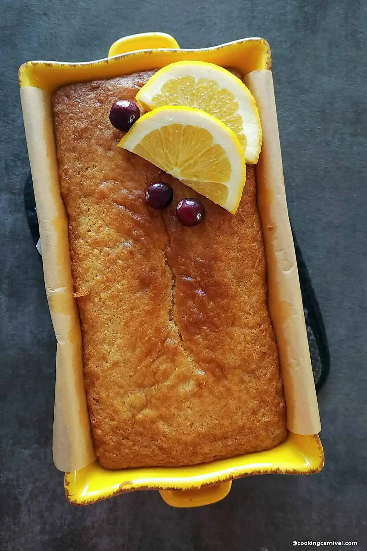 Eggless Orange Cranberry Bread i a loaf pan, decorated with slices or orange and cranberries.