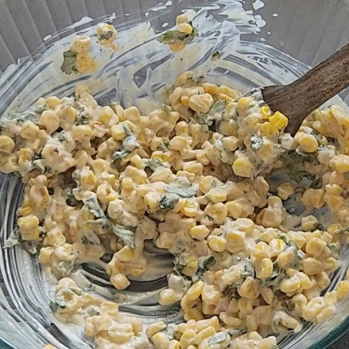 Mixing cooked corn with elote sauce mixture.