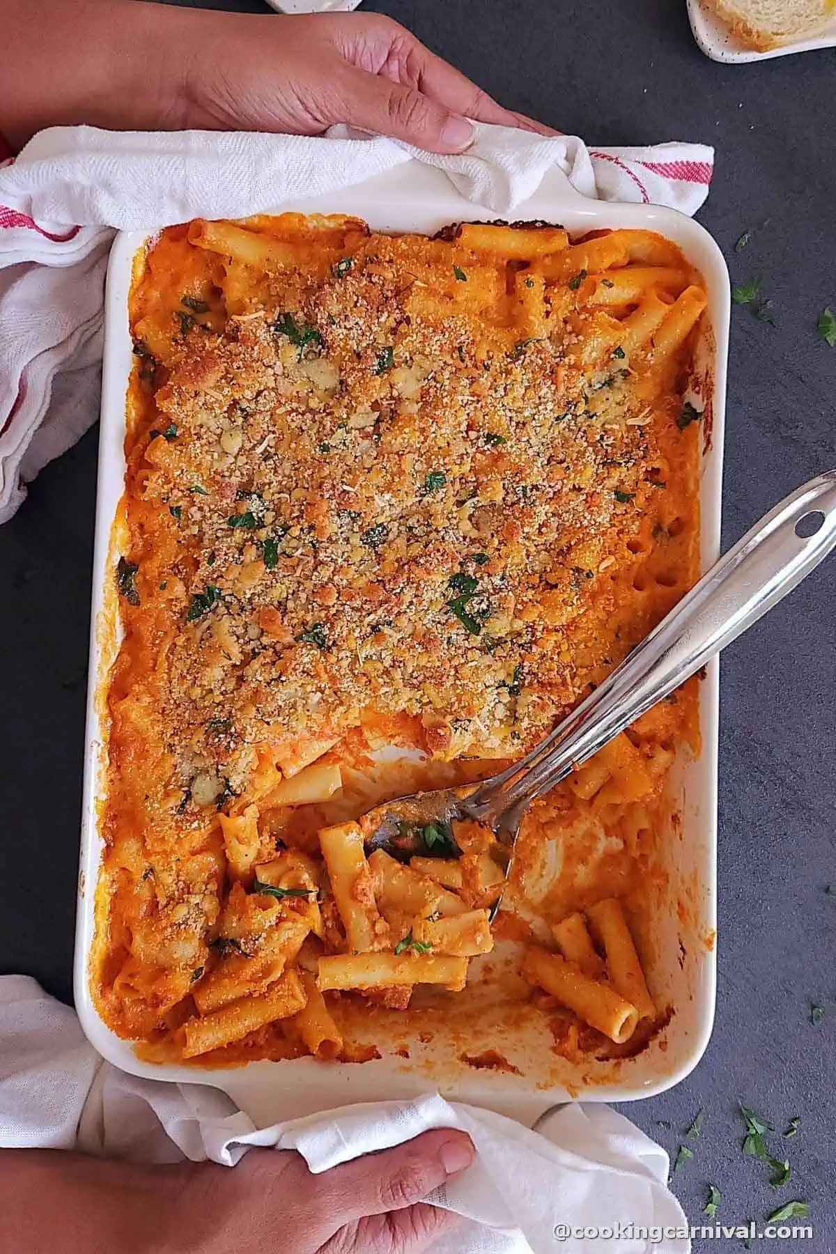 holding baked ziti tray with both the hands.