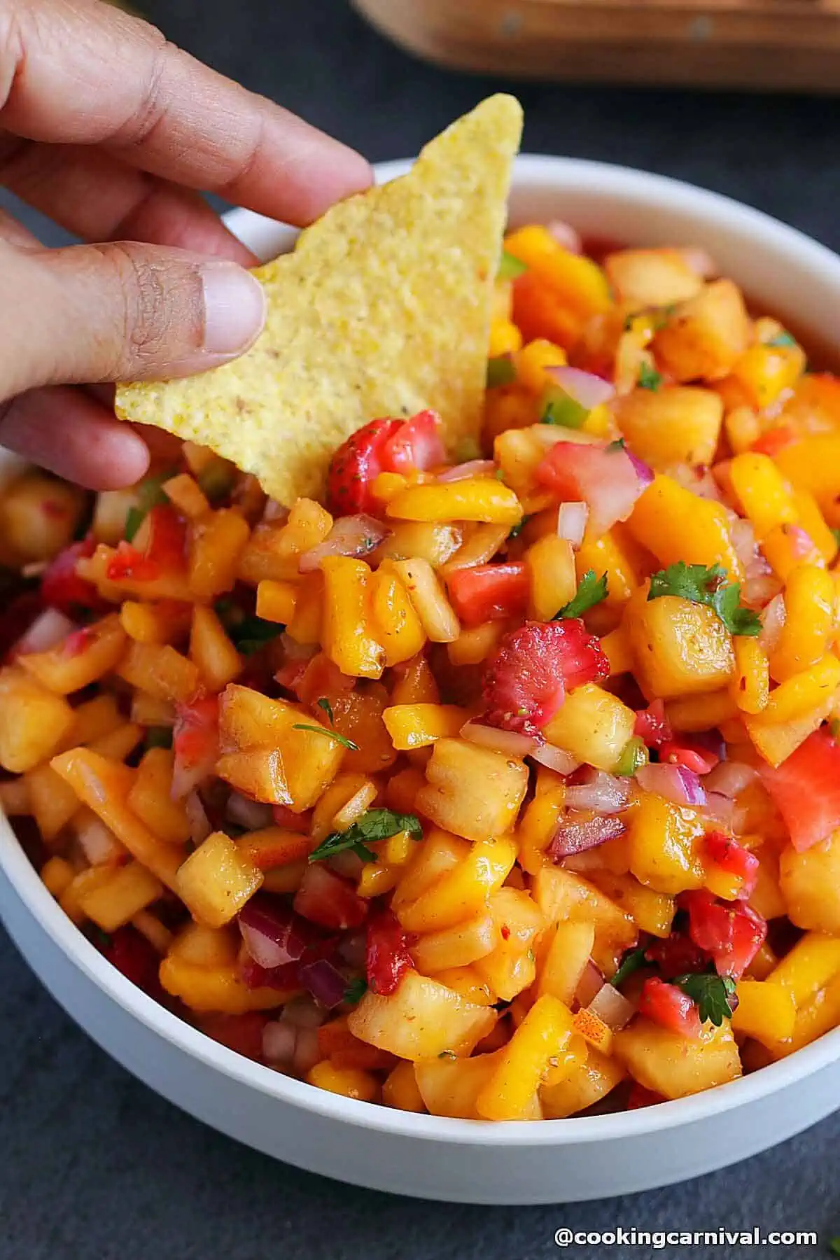 scooping fruit salsa with tortilla chips from white bowl