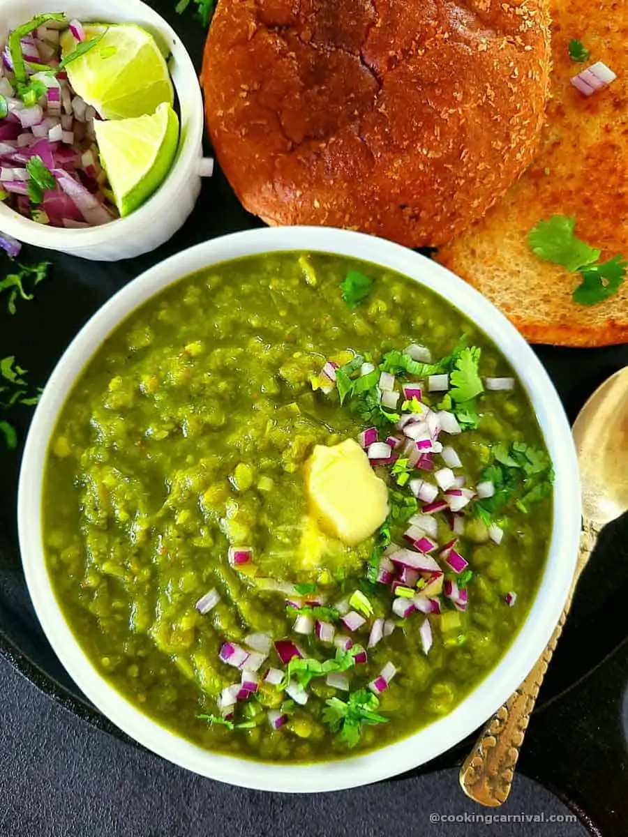 Green pav bhaji in a bowl garnished with butter, onion and cilantro.