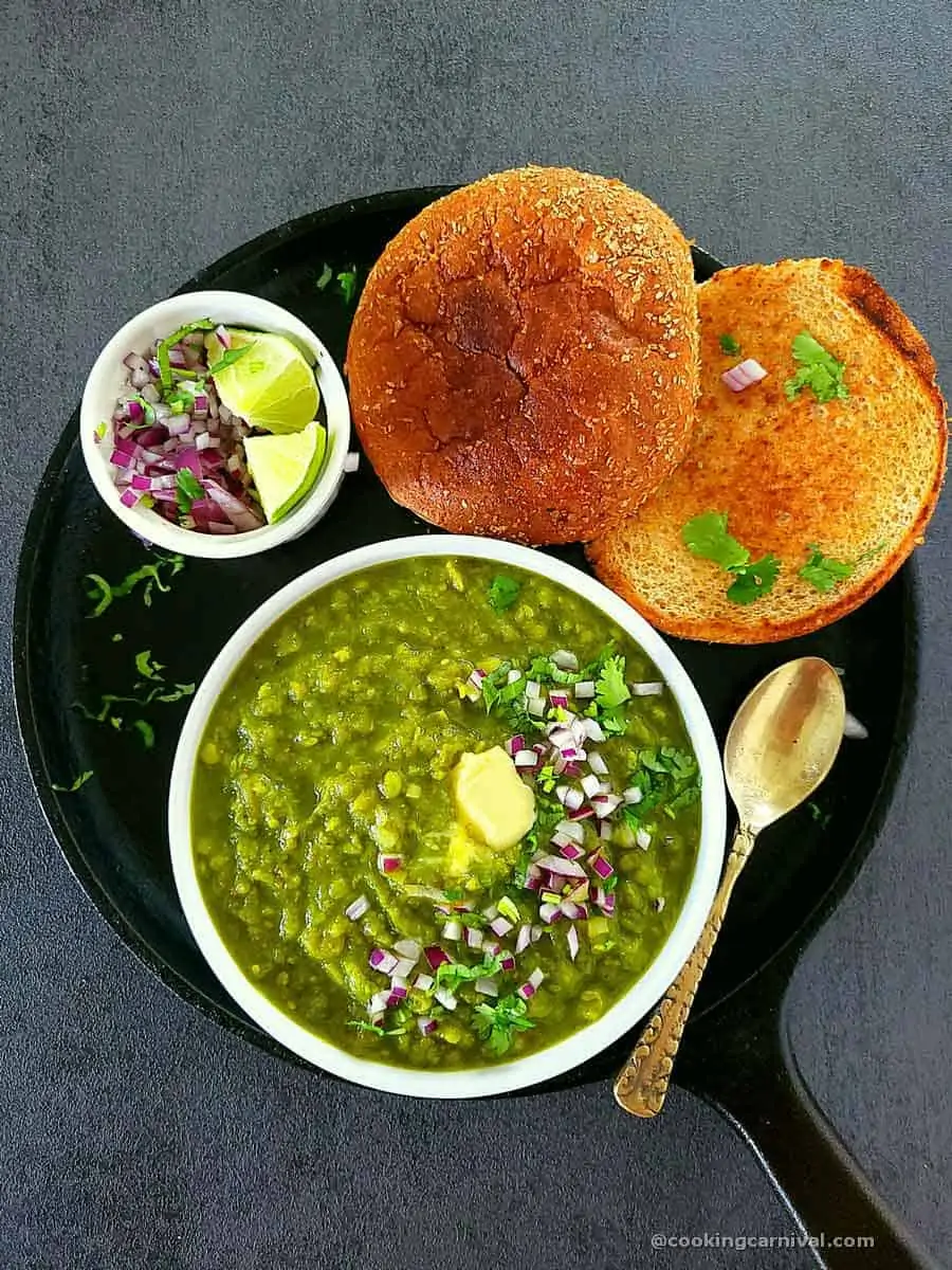 Green pav bhaji in a bowl, onion, cilantro, lime and toasted pav on sides