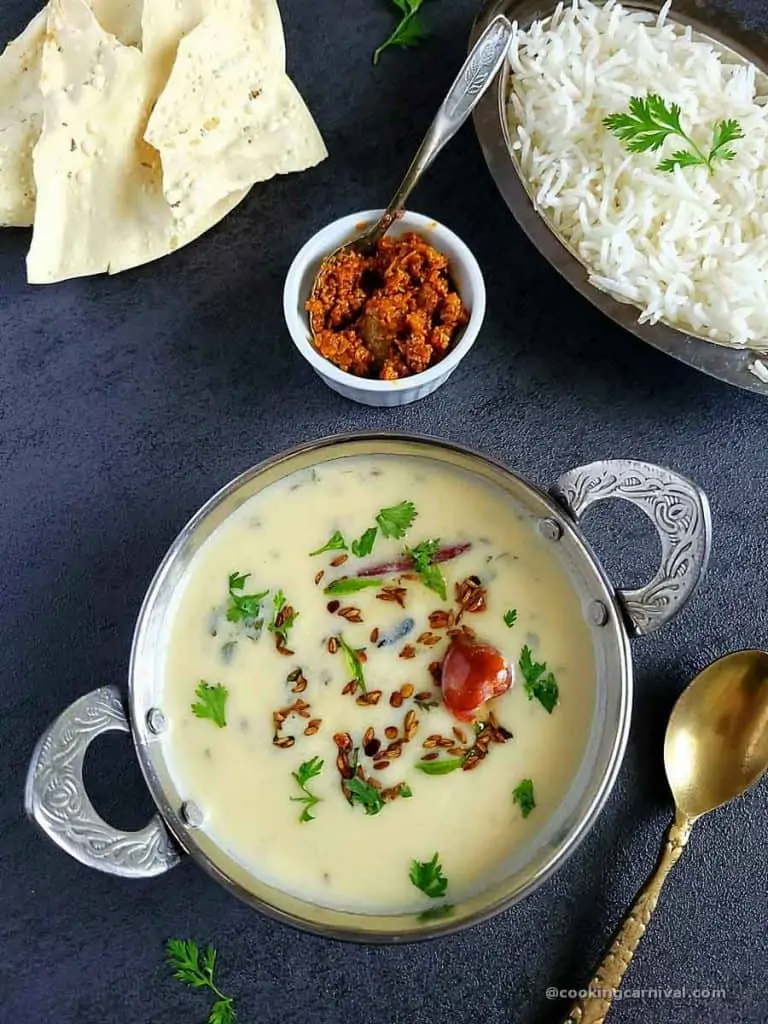 Gujarati kadhiin steel bowl, rice, pickle and papad on sides