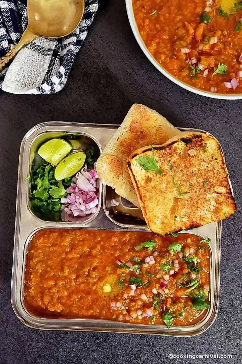 Instant pot pav bhaji on a steel plate with ladi pav, onion, cilantro and lime wedge.