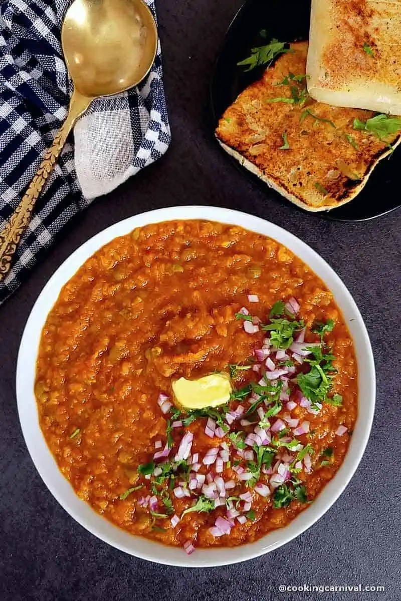 Instant pot pav bhaji served in white bowl, garnished with butter, cilantro, onion and pav.