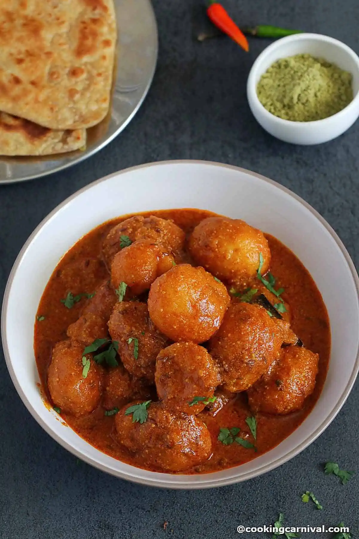 kashmiri dum aloo on a white bowl, paratha on a side.