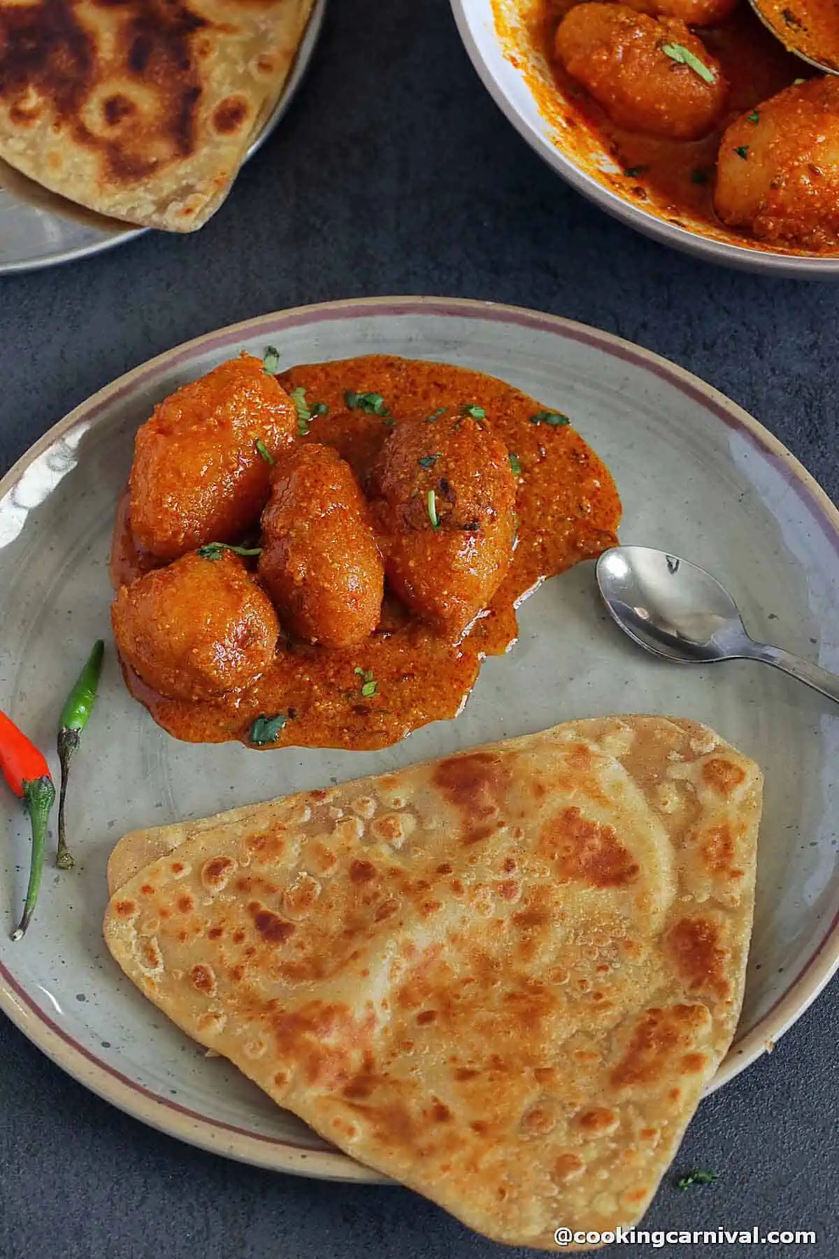 Plain paratha, kashmiri potato curry and green chili on a plate.