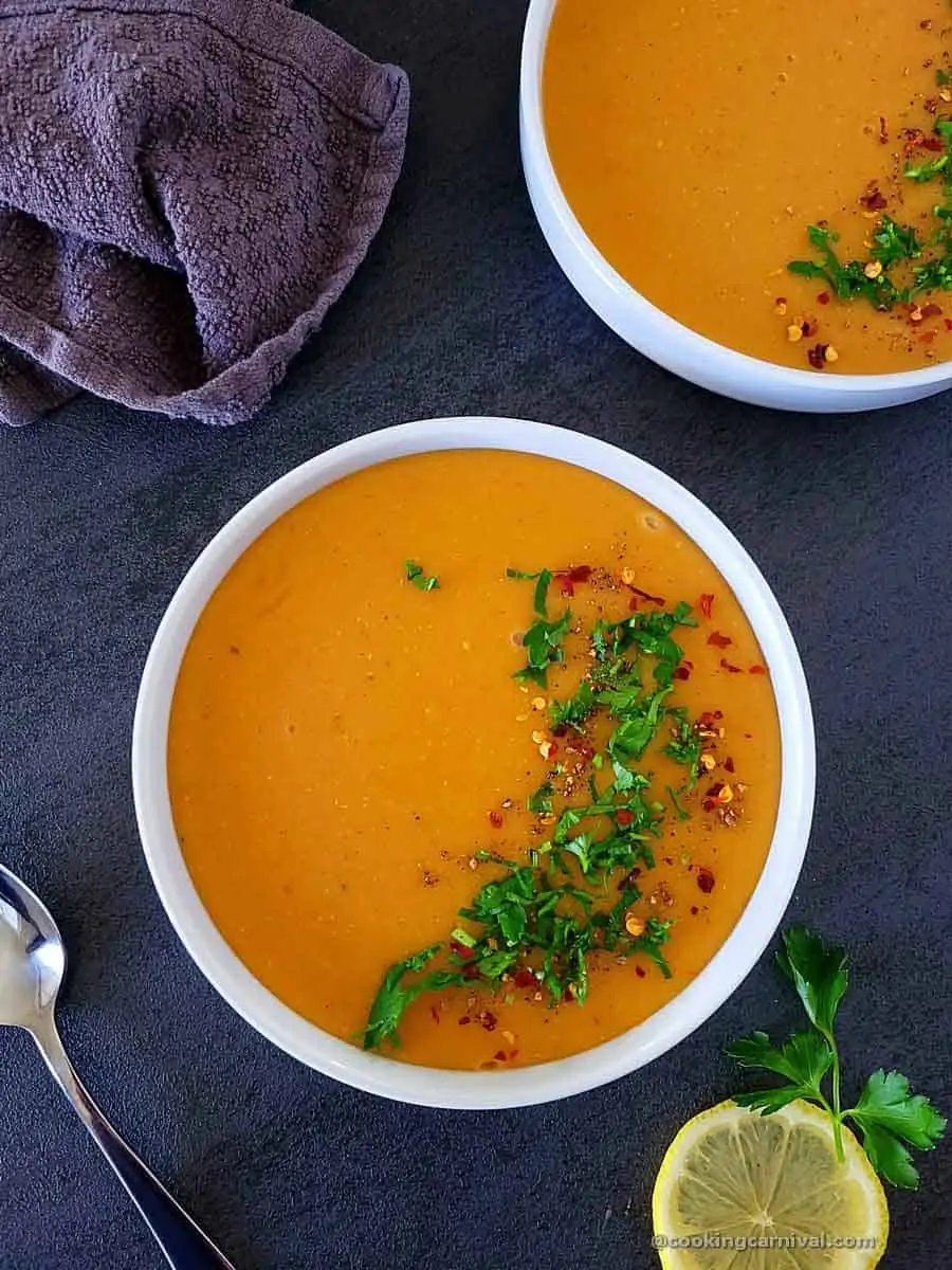 Lebanese lentil soup garnished with parsley, pepper powder and crushed chili, in a white bowl