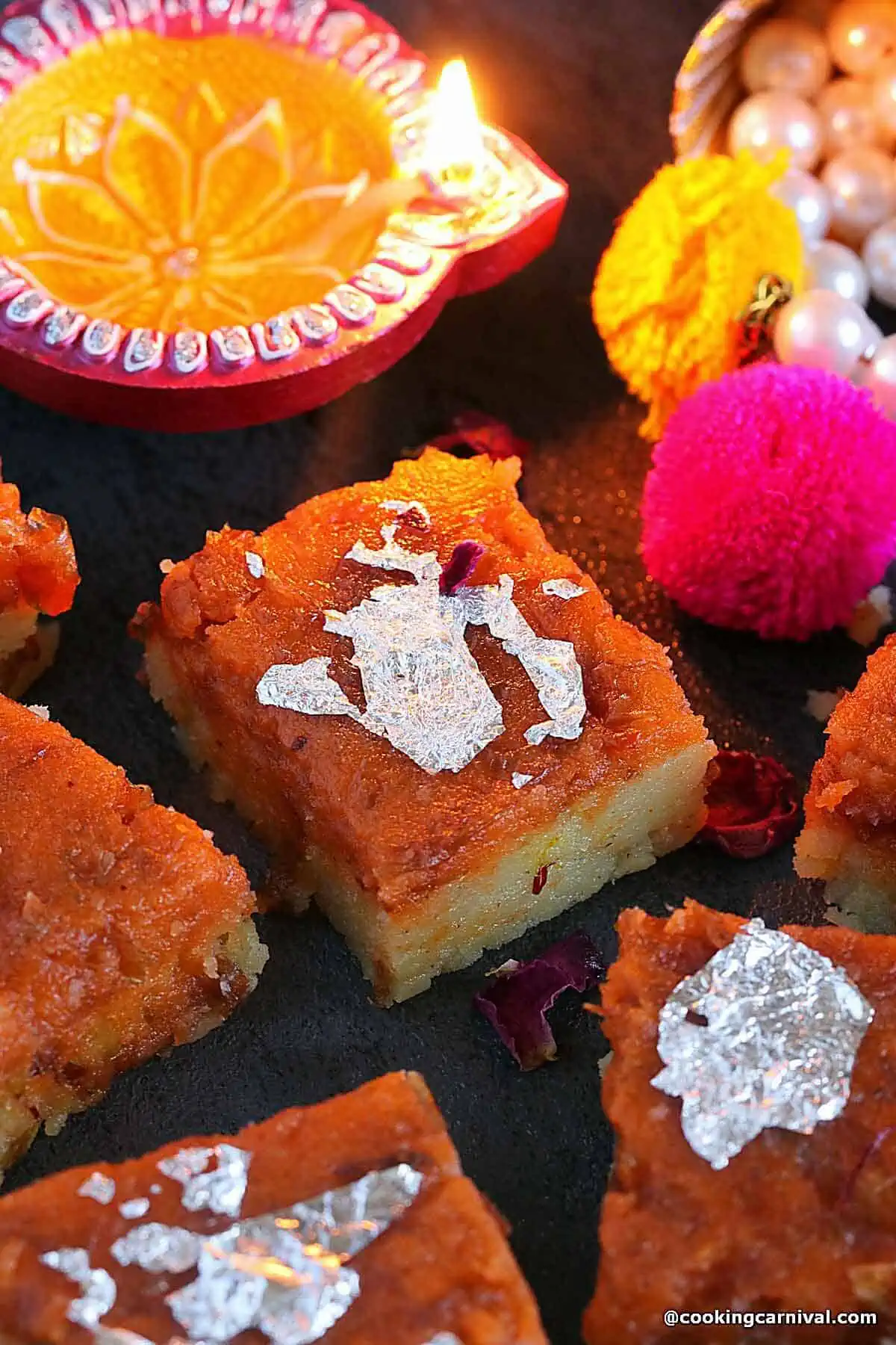 Makhana gulkand burfi on black board, diya and Indian ornaments are placed for decorations.