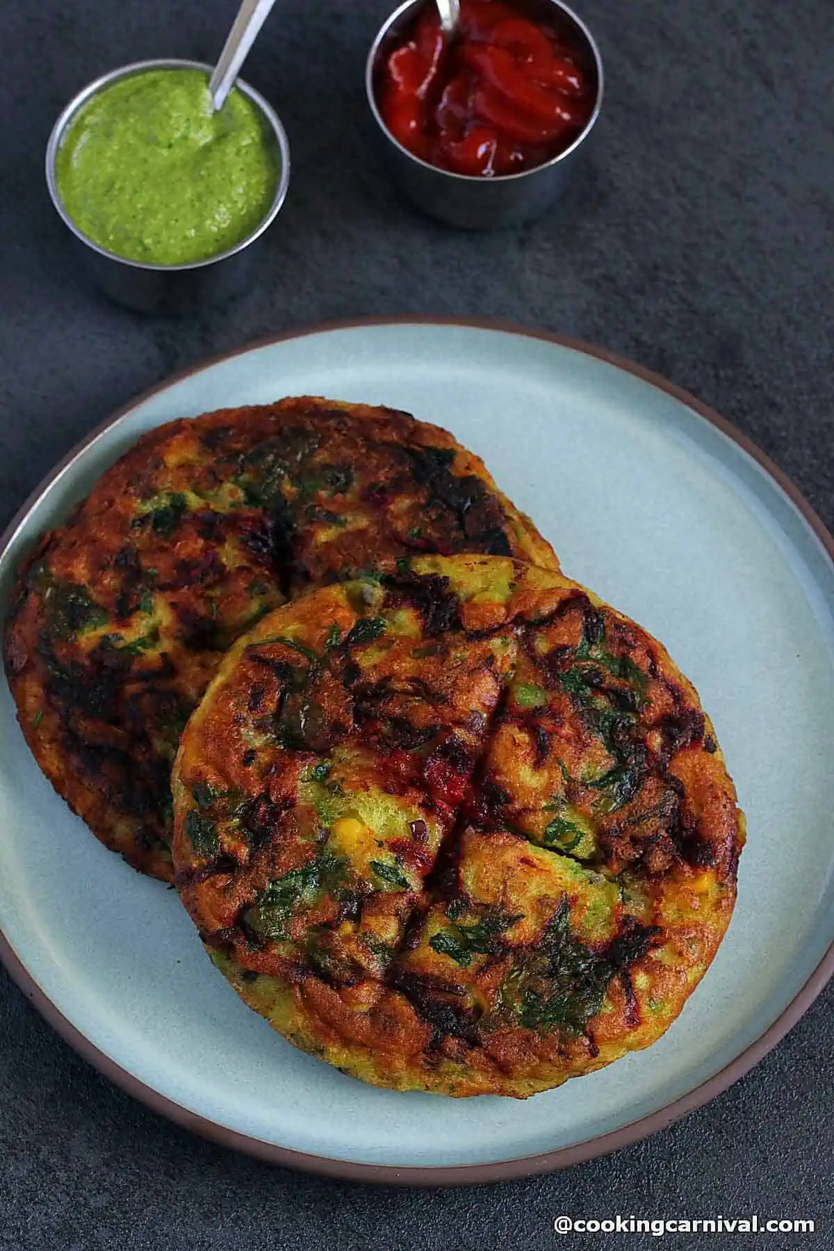 two moonglet (vegetarian omelet) on a plate, green chutney and tomato ketchup on a side.