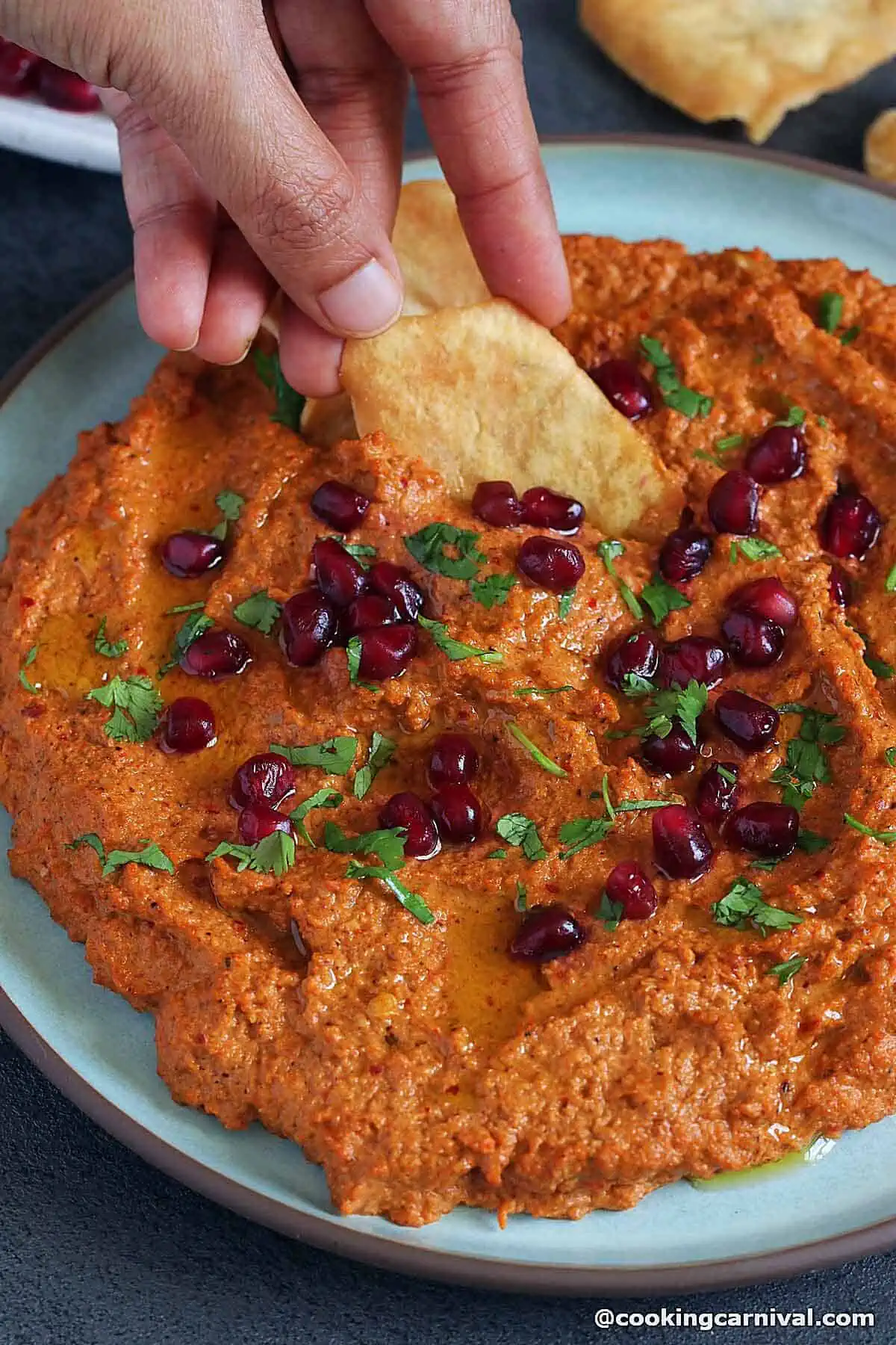 scooping Muhammara dip with pita chips.