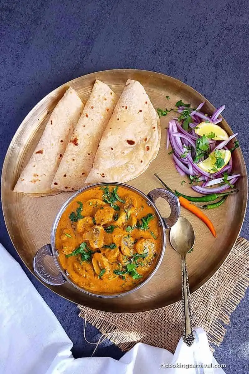 mushroom masala curry served with chapathi, onion and lemon in a kansa plate.