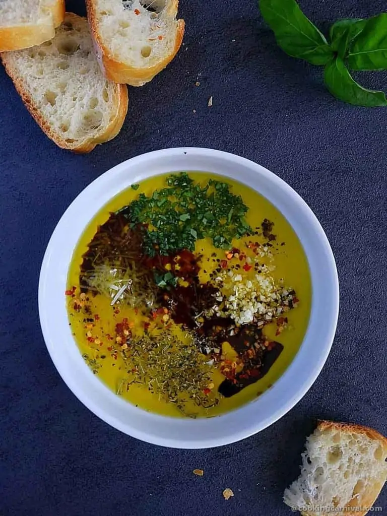 Olive oil dip for bread with fresh and dried hers in a white bowl, crusty bread on a side