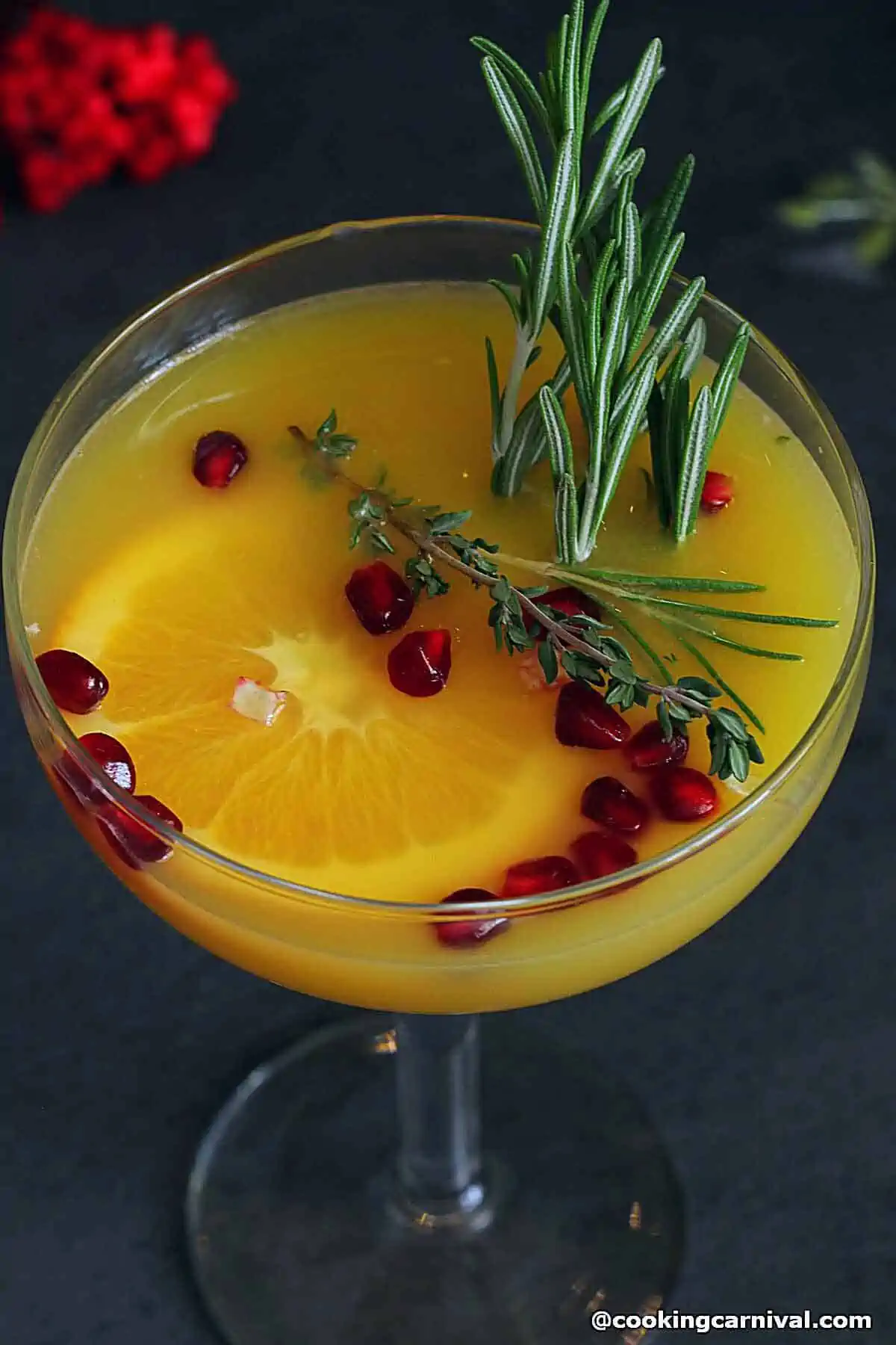 Orange Mocktail in a glass, garnished with rosemary, pomegranate and orange slices.