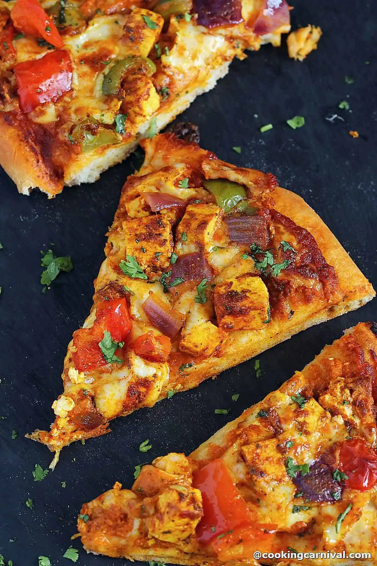 Slices of paneer pizza on black slate. 