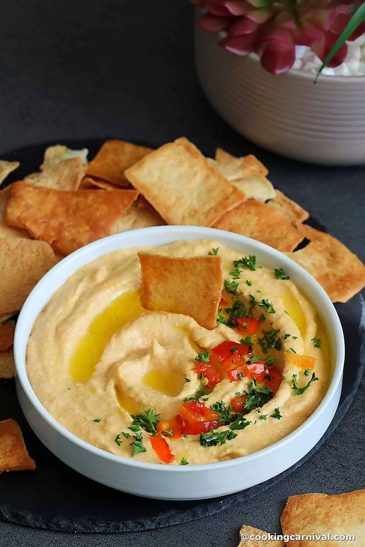 Roasted red pepper hummus in a white bowl, served with pita chips.