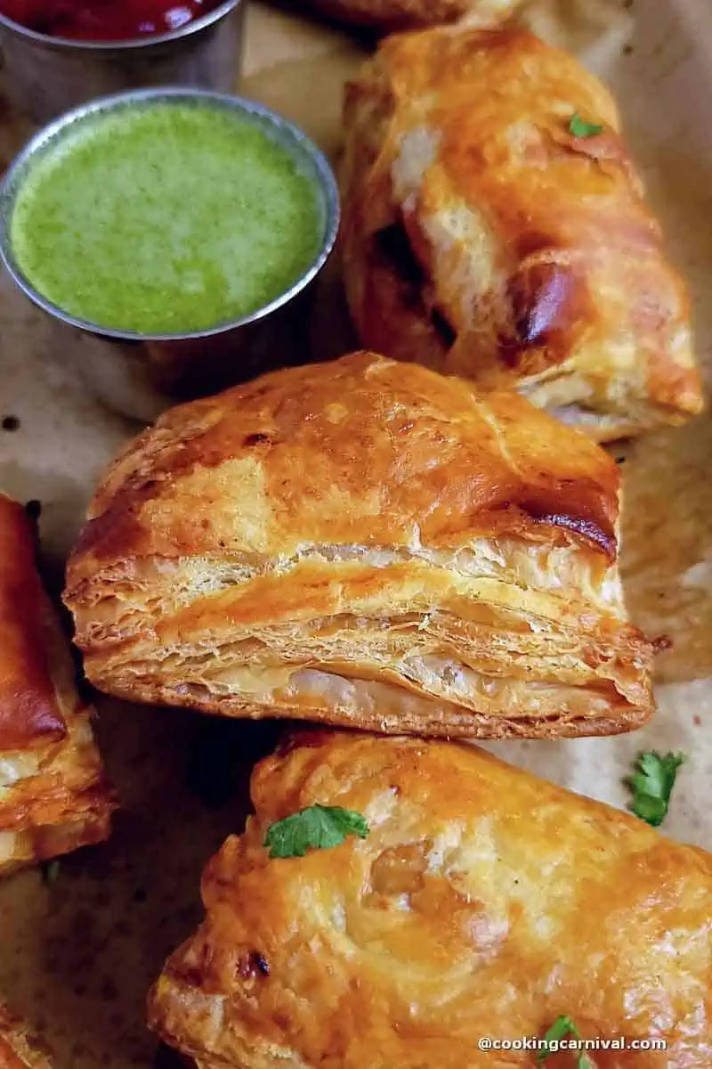 close up shot of flaky baked puffs, green chutney on the side.