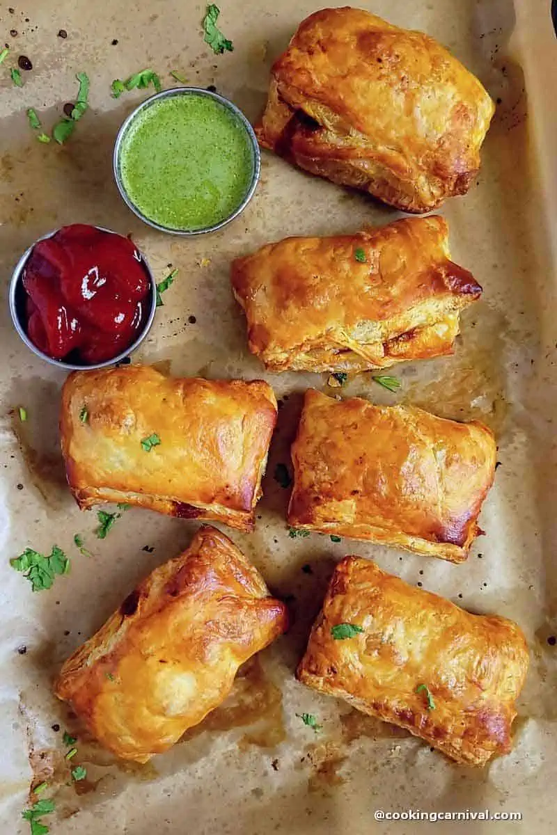 Schezwan Paneer puff on a baking tray served with green chutney and tomato ketchup.