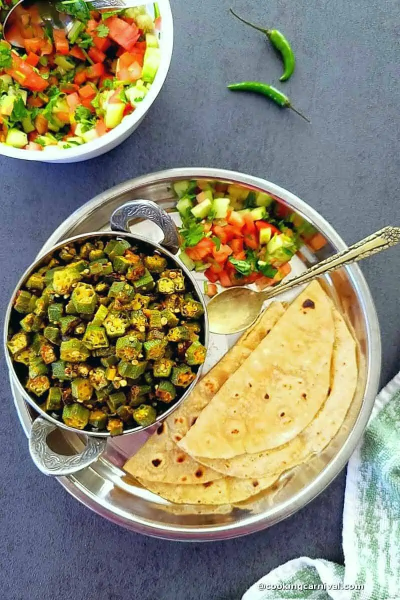 Bhindi masala, roti, salad and green chili in a steel plate